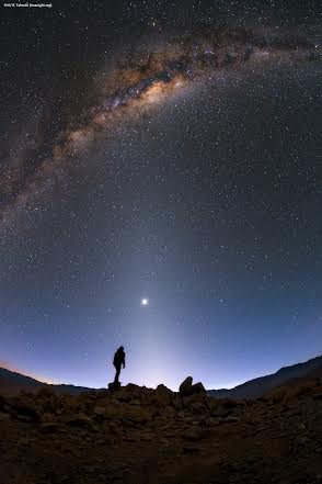 The faint light extending up from the horizon just below centre of this photo is known as zodiacal light, caused by sunlight scattering from cosmic dust in the plane of our Earth’s orbit. A second band of light can be seen at the horizon on the lower left. This red light is airglow, produced by the Earth’s atmosphere. Airglow is caused by processes taking place in the upper atmosphere, including cosmic rays, recombining photoionized atoms, and various chemical reactions between oxygen, nitrogen, hydroxyl, sodium, and lithium atoms. The third and final band is the Milky Way, our home galaxy, high in the sky. This band consists of billions of stars of all kinds. Many of them are hidden to the human eye behind large layers of interstellar dust, giving the Milky Way its characteristically mottled look. At the centre of the image stands ESO Photo ambassador Babak Tafreshi, watching the light spectacle unfold around him. His fellow photo ambassador Yuri Beletsky captured this image during the ESO UHD Expedition in 2014, as Babak travelled through the Chilean desert to visit the sites of ESO’s telescopes.